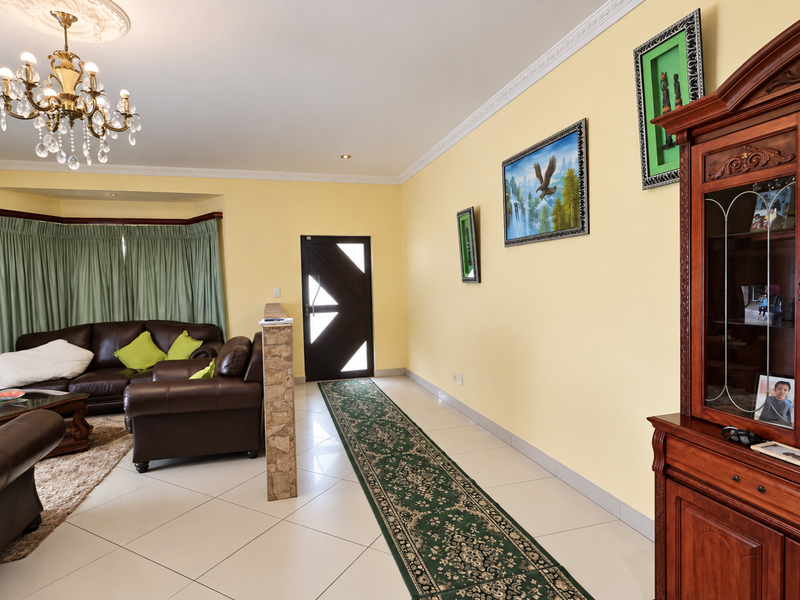 Spacious living area featuring tiled floors, decorative crown molding, a crystal chandelier, and a stone-accented partition wall near the front entrance.