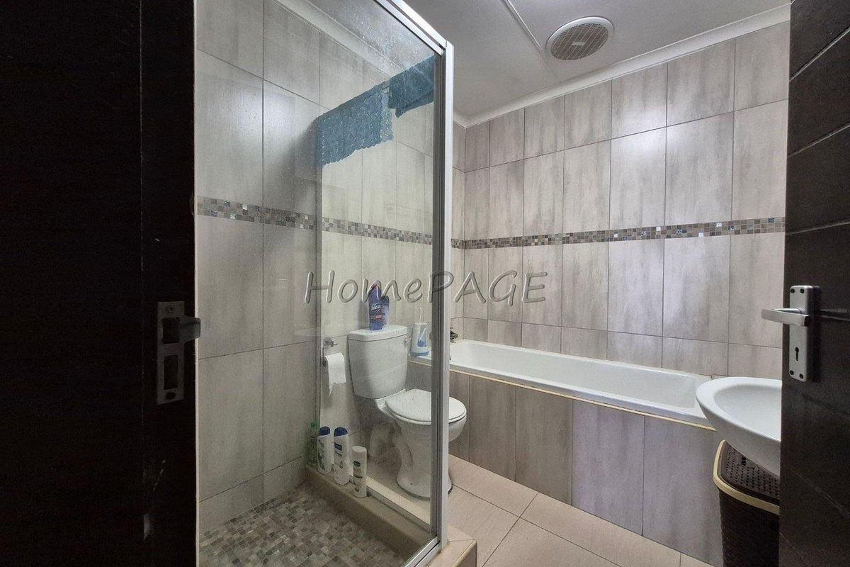 A functional bathroom featuring a glass-enclosed shower, a built-in bathtub, a toilet, and a wall-mounted basin with neutral wall and floor tiling.