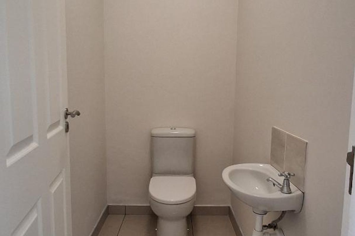 A clean and functional guest bathroom featuring a modern toilet and a wall-mounted basin with tiled flooring.
