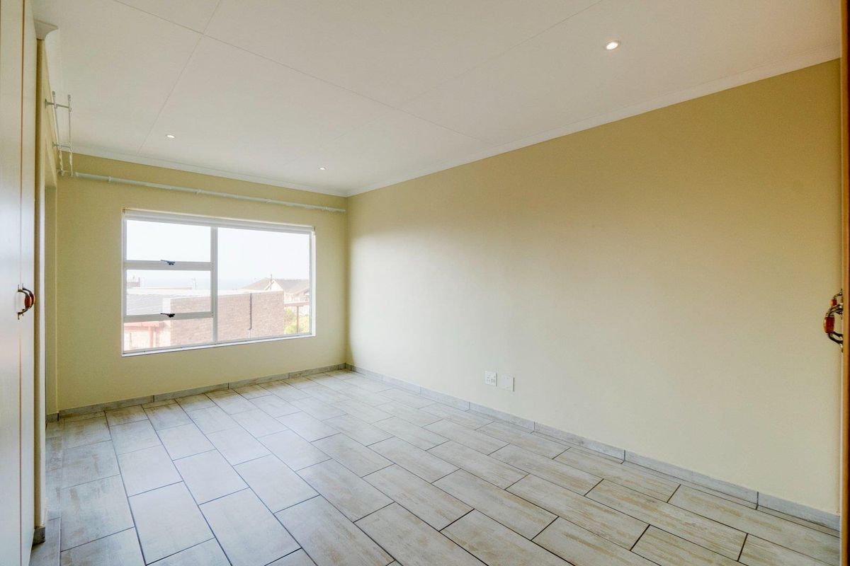A bright, empty bedroom featuring neutral walls, tiled flooring, recessed ceiling lighting, and a large window providing natural light.
