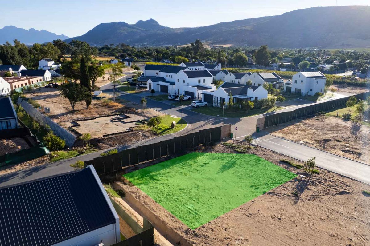 An aerial view of a vacant residential plot in a developed estate, featuring road access and surrounding mountain views.