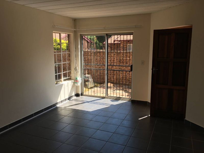 An empty living room featuring tiled flooring, a sliding glass door with security gate, and access to an outdoor area.