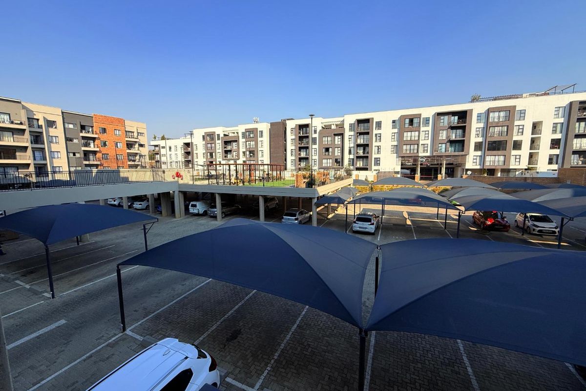 An elevated view of the apartment complex parking area featuring paved surfaces and multiple shade-cloth carports.