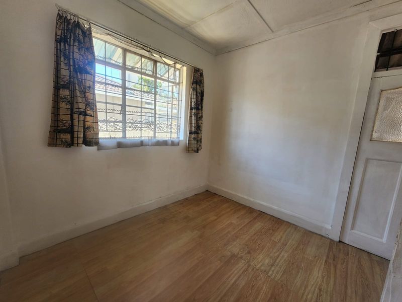 An empty bedroom featuring laminate flooring, security bars on the window, and a traditional timber door.