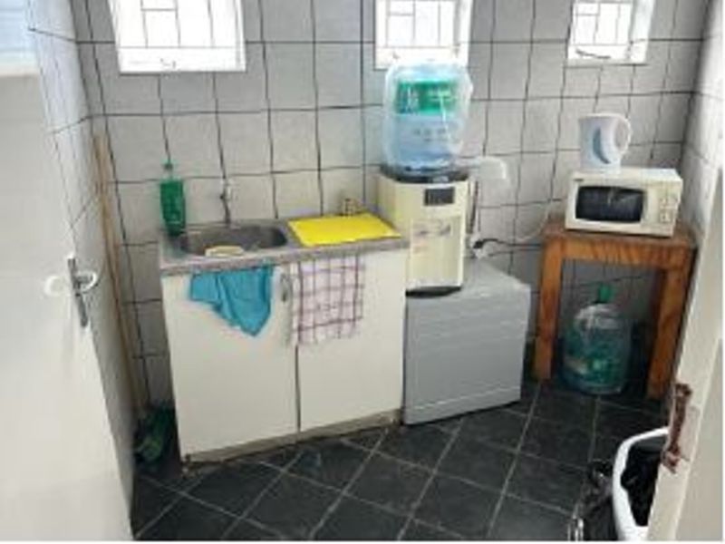 A small kitchenette area featuring a stainless steel sink, built-in base cabinetry, and tiled wall and floor finishes.