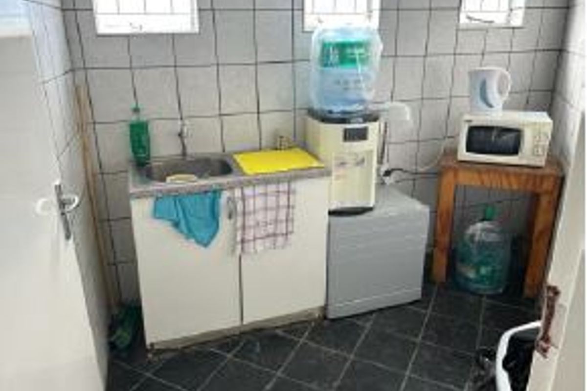 A small kitchenette area featuring a stainless steel sink, built-in base cabinetry, and tiled wall and floor finishes.