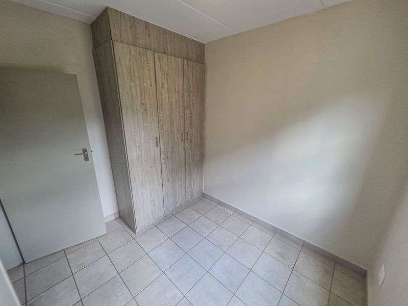 A clean, empty bedroom featuring neutral tiled flooring and built-in wooden cupboards, offering a blank canvas for personalization.