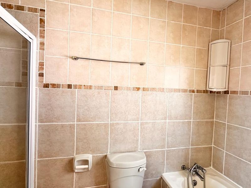 A functional bathroom featuring a shower enclosure, bathtub, and neutral wall tiling, offering a clean space ready for potential cosmetic updates.