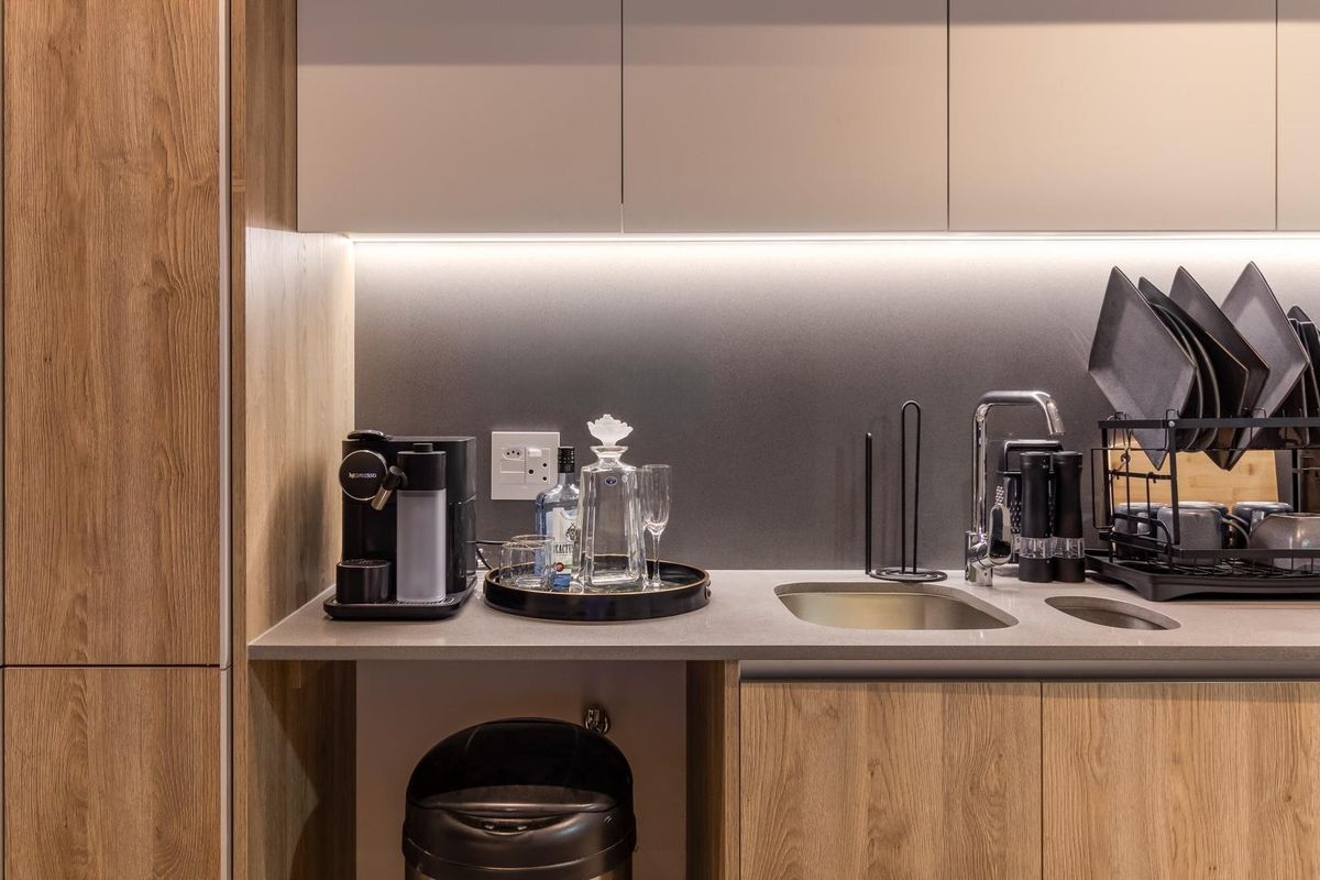 Modern kitchen kitchenette area featuring sleek wood-grain cabinetry, stone countertops, integrated sink, and under-cabinet LED lighting.