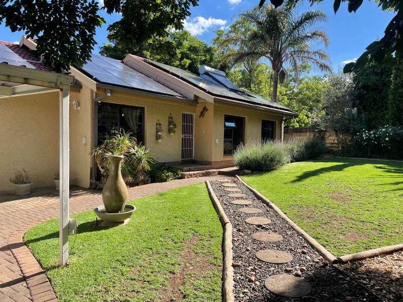 Rear view of the house featuring a well-maintained garden, paved pathways, and installed solar energy infrastructure on the roof.