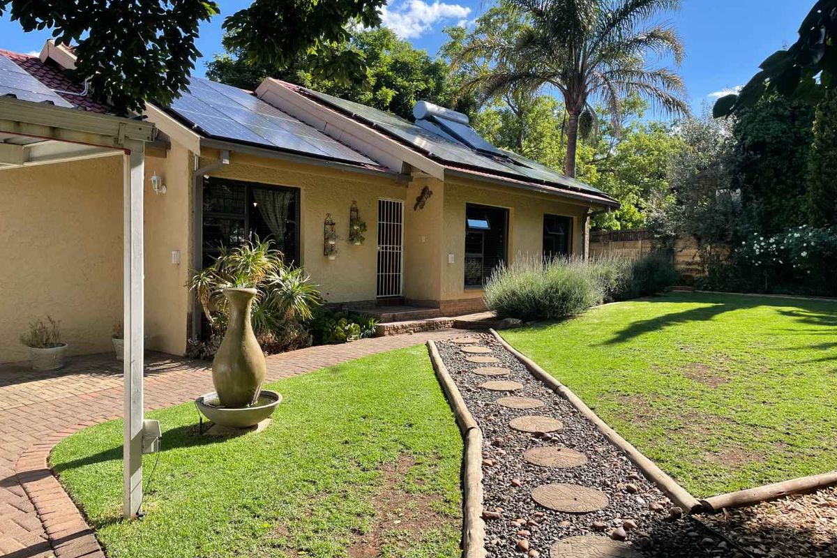Rear view of the house featuring a well-maintained garden, paved pathways, and installed solar energy infrastructure on the roof.