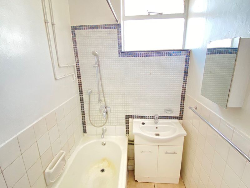 Compact bathroom featuring a bathtub with shower mixer, vanity basin, and tiled wall finishes. The space is functional but would benefit from cosmetic updates.