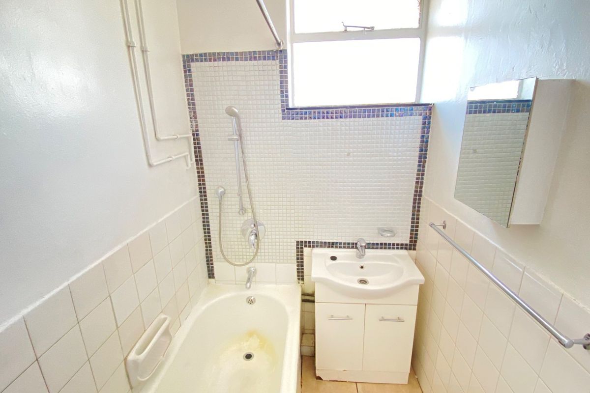 Compact bathroom featuring a bathtub with shower mixer, vanity basin, and tiled wall finishes. The space is functional but would benefit from cosmetic updates.