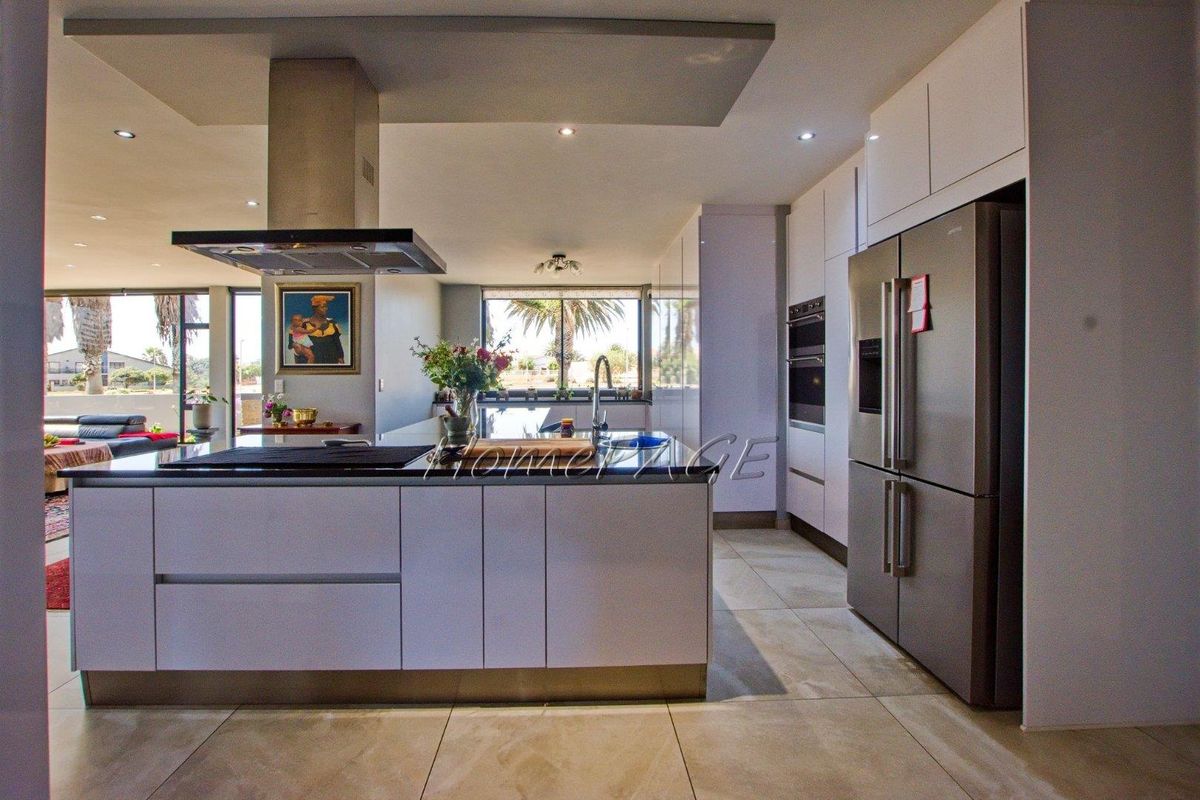 Modern open-plan kitchen featuring a central island, sleek cabinetry, built-in appliances, and high-quality tiled flooring with ample natural light.