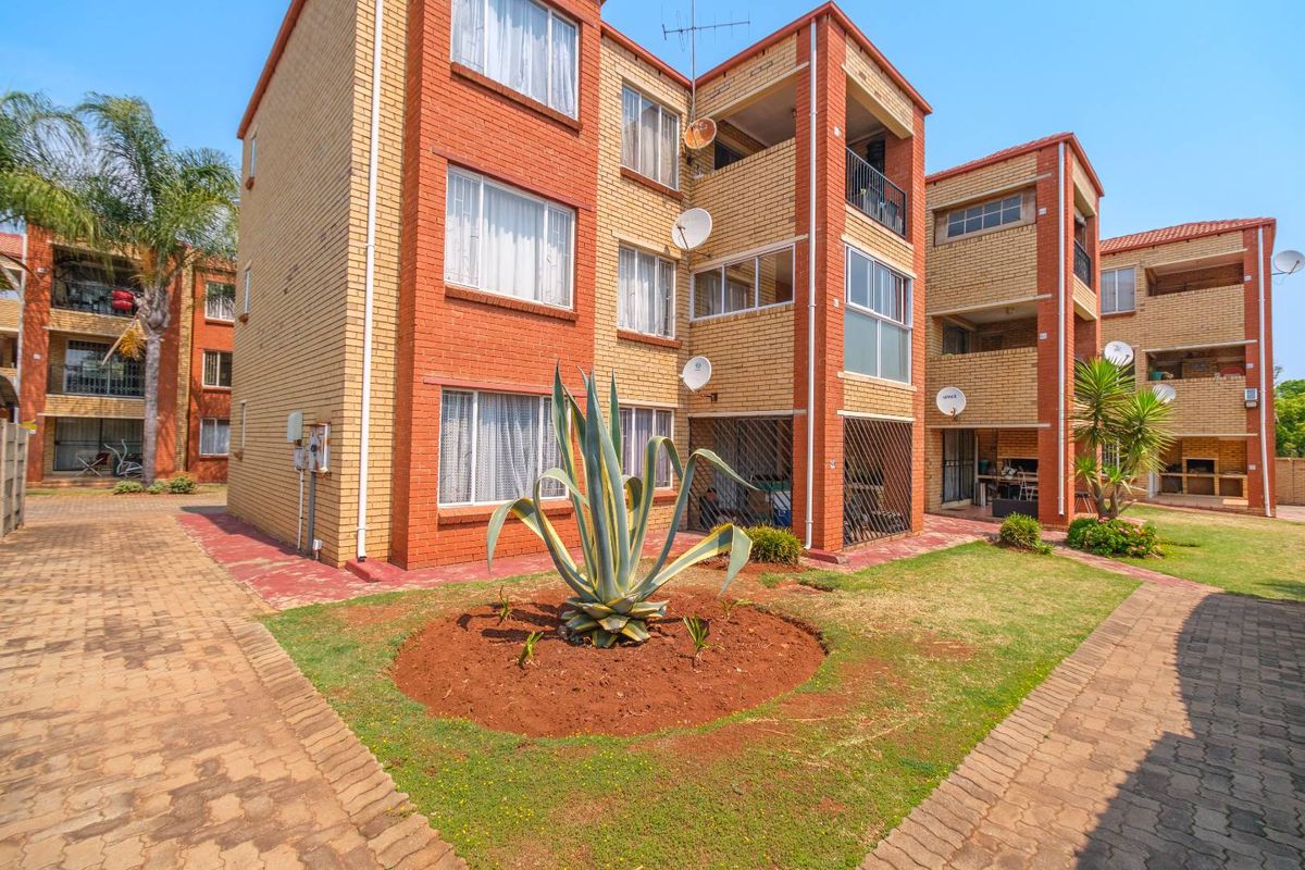 Rear view of a multi-story brick apartment complex featuring paved common areas, balconies, and established landscaping.