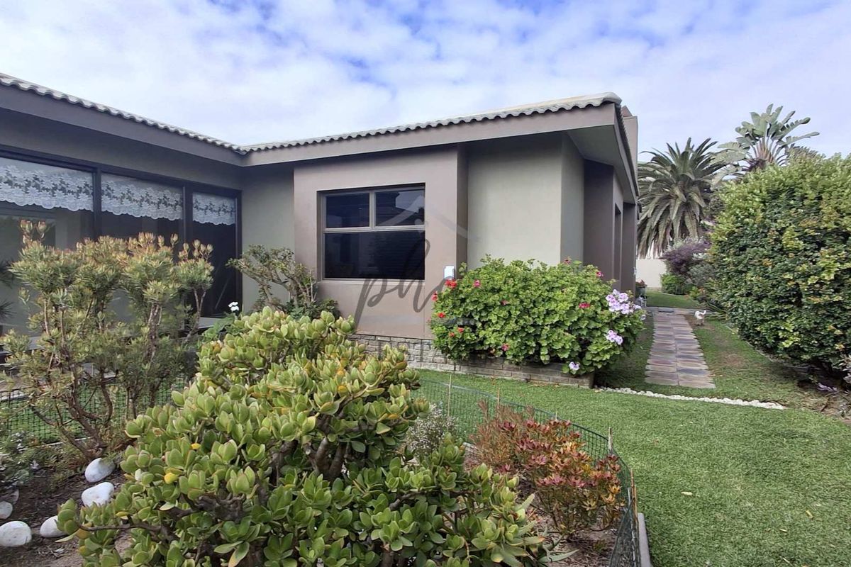 A well-maintained rear exterior view of the house featuring a landscaped garden, paved walkway, and sliding glass doors leading to the interior.