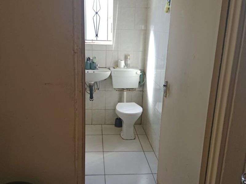 A compact bathroom featuring tiled walls and floors, a pedestal basin, and a standard toilet, requiring cosmetic updates to improve its overall condition.