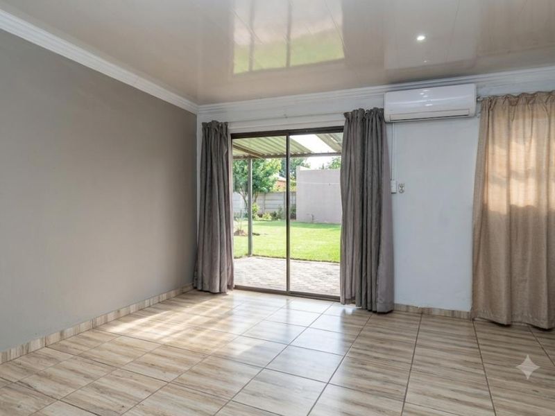 A bright, empty living room featuring tiled flooring, a split-system air conditioner, and sliding glass doors providing direct access to the rear garden.