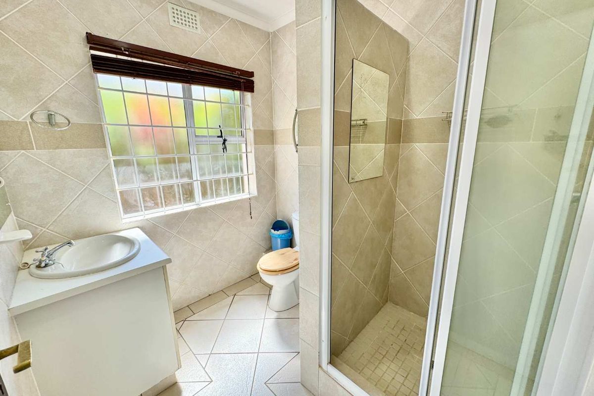 A functional bathroom featuring a glass-enclosed shower, a built-in vanity with a basin, and tiled walls and flooring.