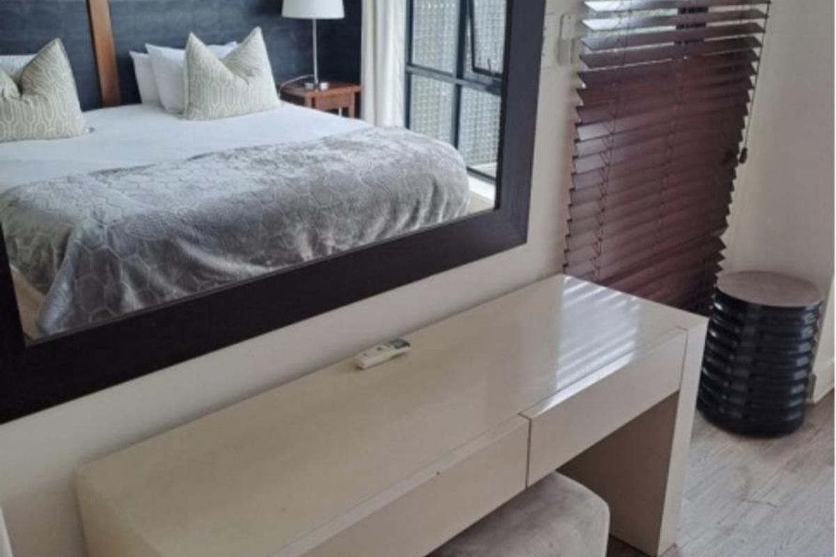 A well-maintained bedroom featuring laminate flooring, a large wall-mounted mirror, and a window fitted with wooden venetian blinds.