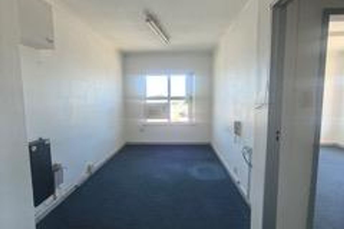 An empty office space featuring blue carpeting, fluorescent lighting, and a wall-mounted heater, suitable for a professional workspace.