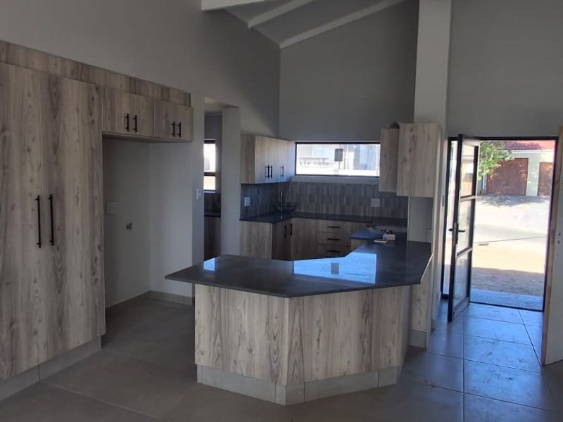 Modern kitchen featuring light wood-grain cabinetry, dark stone countertops, and a vaulted ceiling, offering a clean and functional open-plan layout.