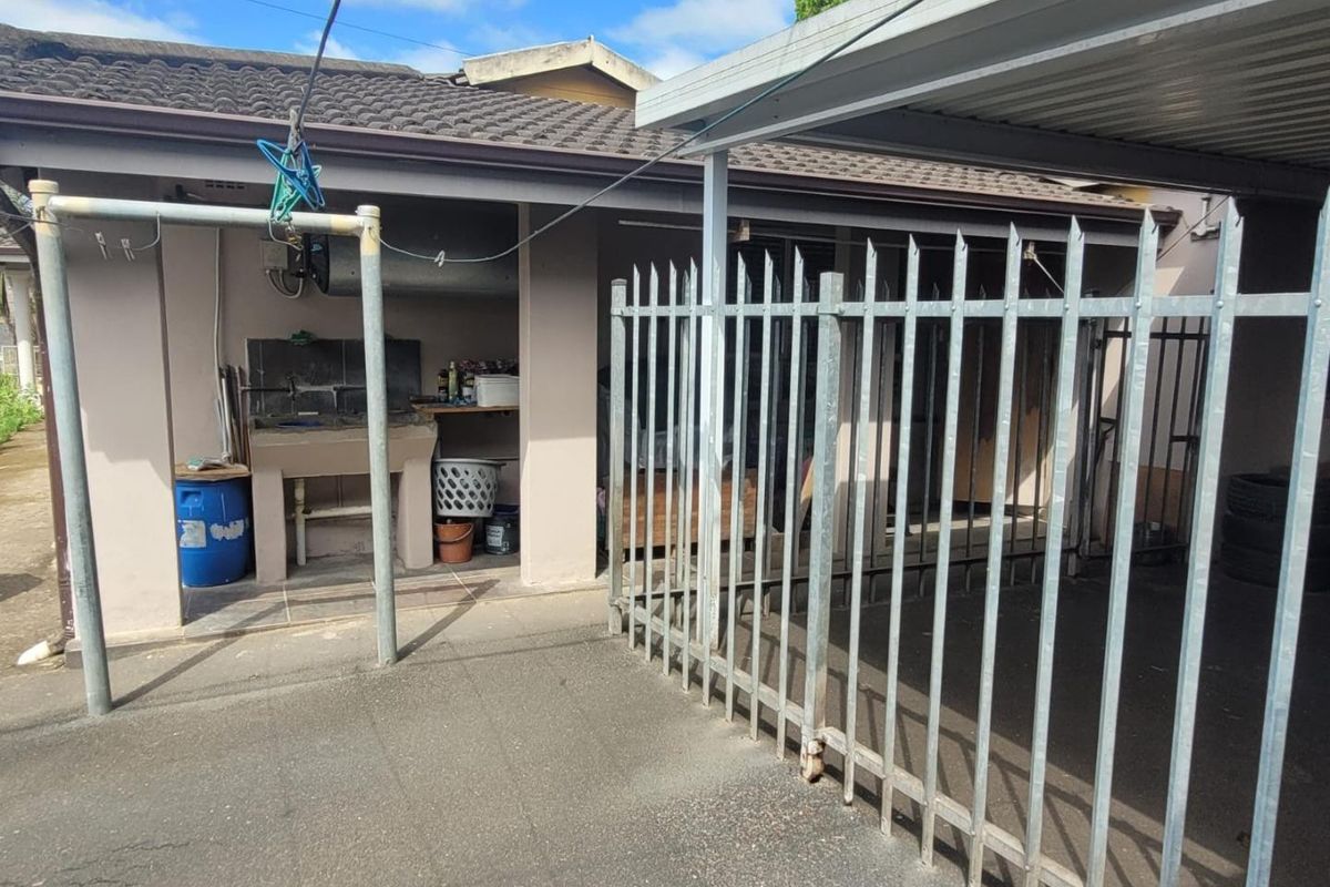 Rear exterior area featuring a concrete wash basin, metal security fencing, and a covered carport structure.