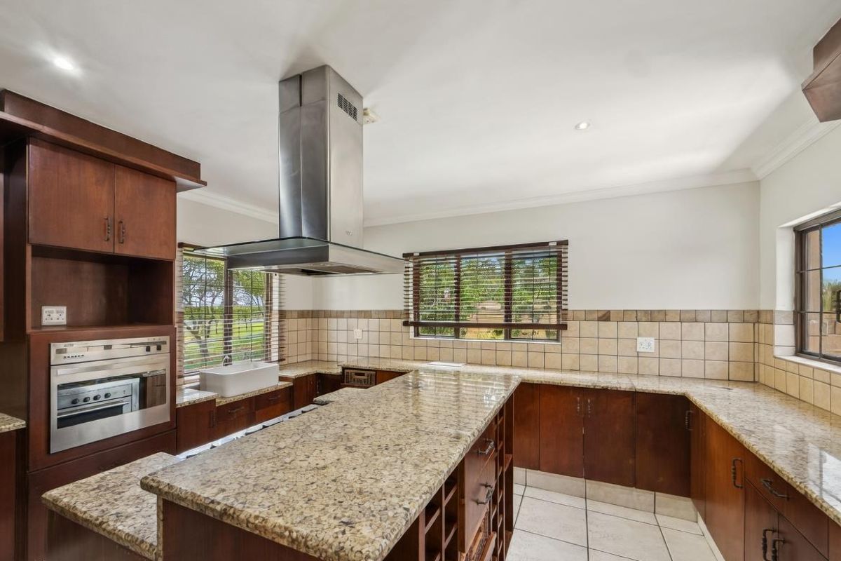 Spacious kitchen featuring granite countertops, dark wood cabinetry, a central island, stainless steel extractor fan, and built-in oven.