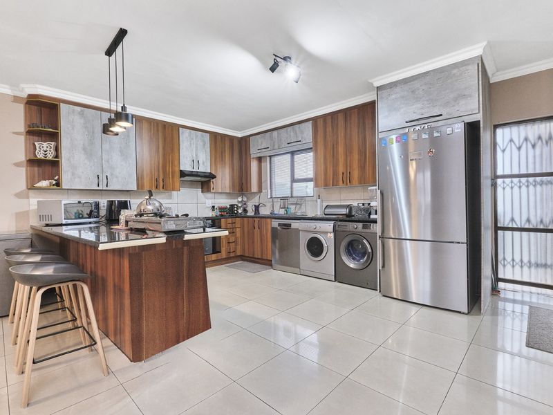 Modern kitchen featuring wood-tone and grey cabinetry, granite countertops, a breakfast bar, and integrated appliance spaces with tiled flooring throughout.