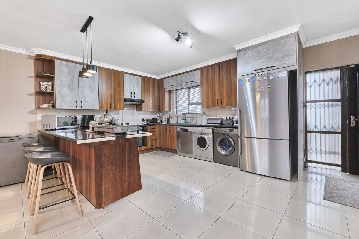 Modern kitchen featuring wood-tone and grey cabinetry, granite countertops, a breakfast bar, and integrated appliance spaces with tiled flooring throughout.