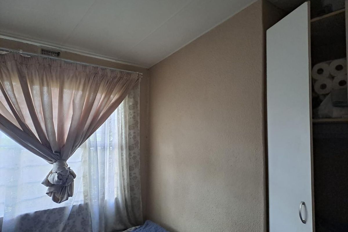A bedroom featuring a built-in wardrobe and a window with curtain fixtures, showing signs of wear on the wall finishes.