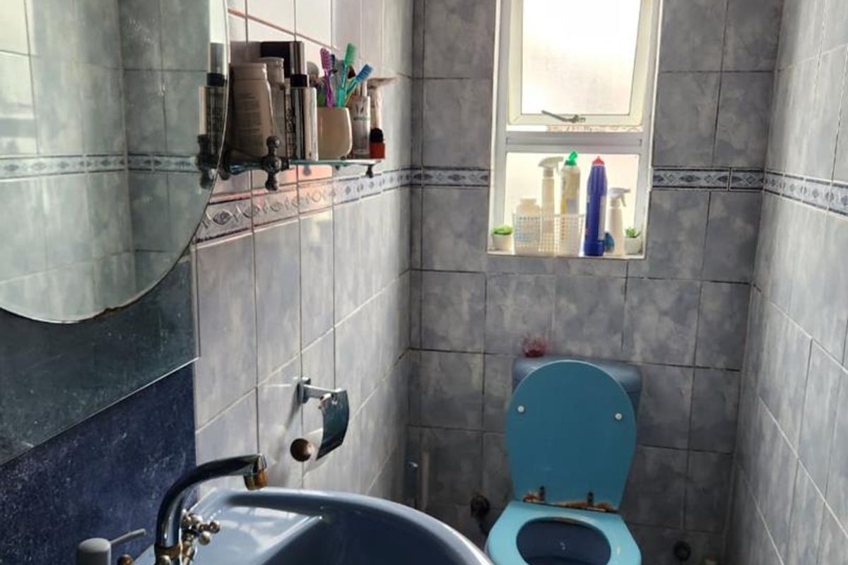 A compact bathroom featuring blue sanitaryware, fully tiled walls, and a small window, presenting an opportunity for modernization.