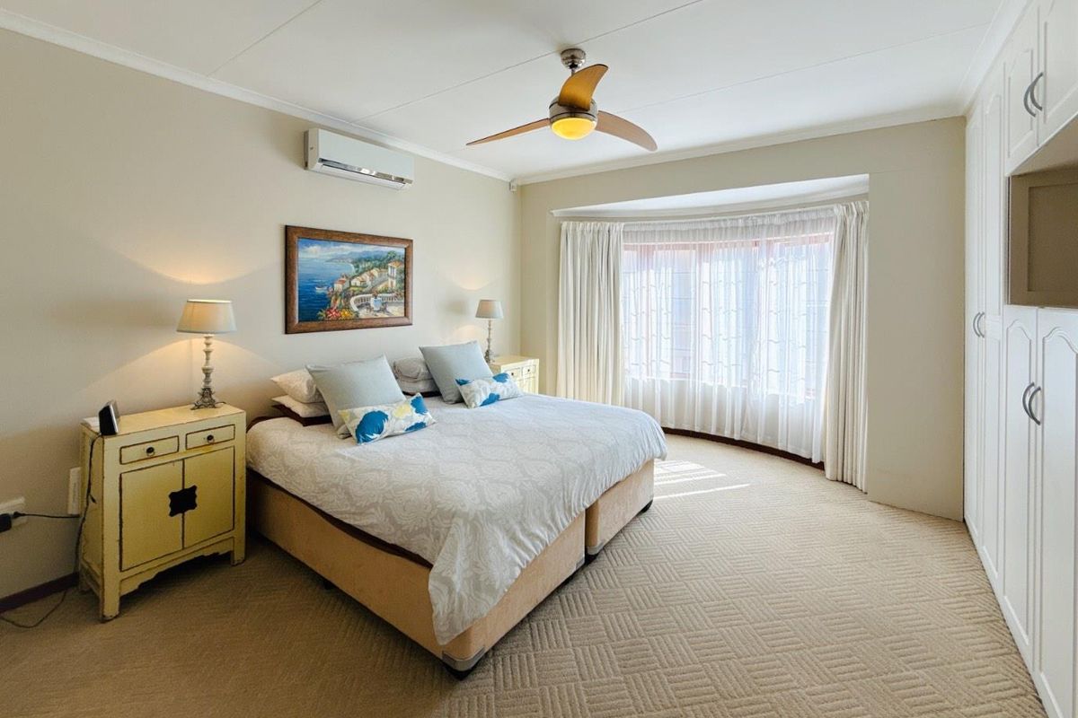 Spacious bedroom featuring neutral carpeting, built-in cupboards, a ceiling fan, and a wall-mounted air conditioning unit for climate control.