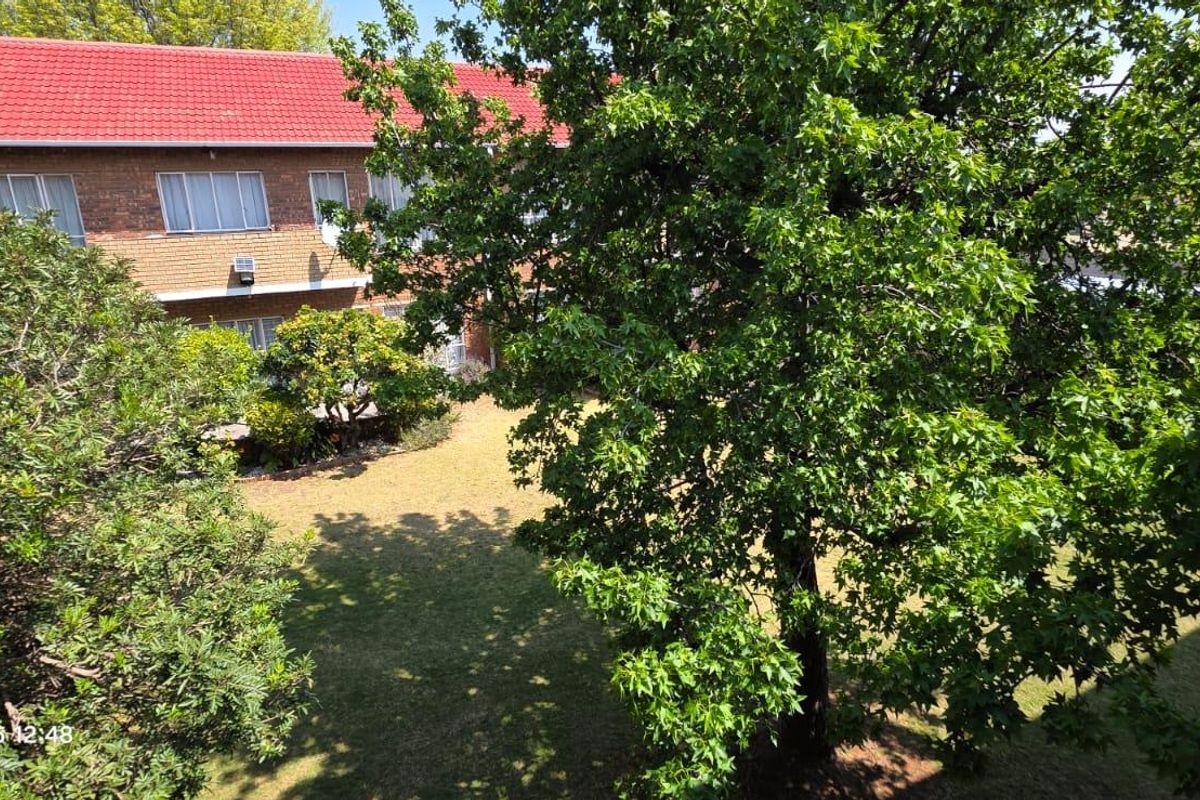 View of the apartment building exterior featuring a brick facade, tiled roof, and surrounding garden area.