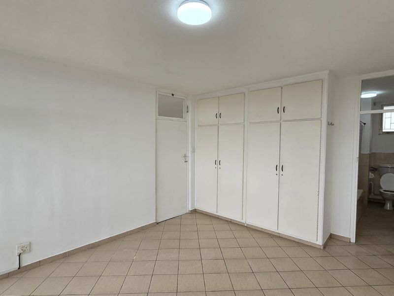 A vacant bedroom featuring neutral tiled flooring, ample built-in cupboard storage, and direct access to an en-suite bathroom.