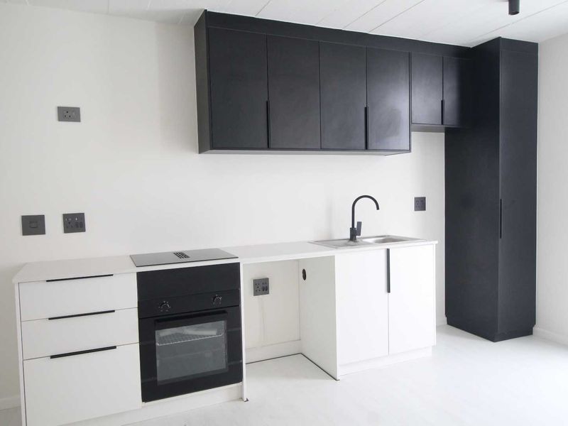 A modern, minimalist kitchen featuring high-contrast black and white cabinetry, a built-in oven, electric hob, and a sleek sink area.