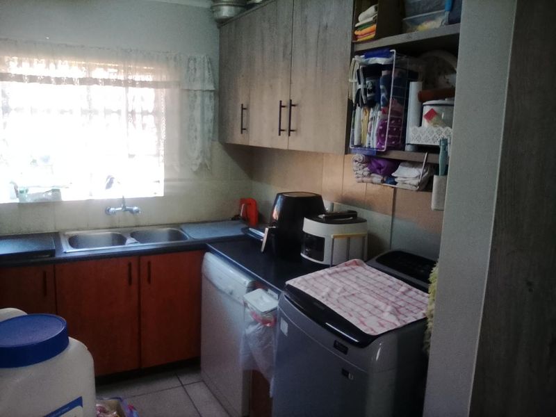 A functional kitchen area featuring laminate cabinetry, double bowl sink, and tiled splashback, providing essential utility and storage space.