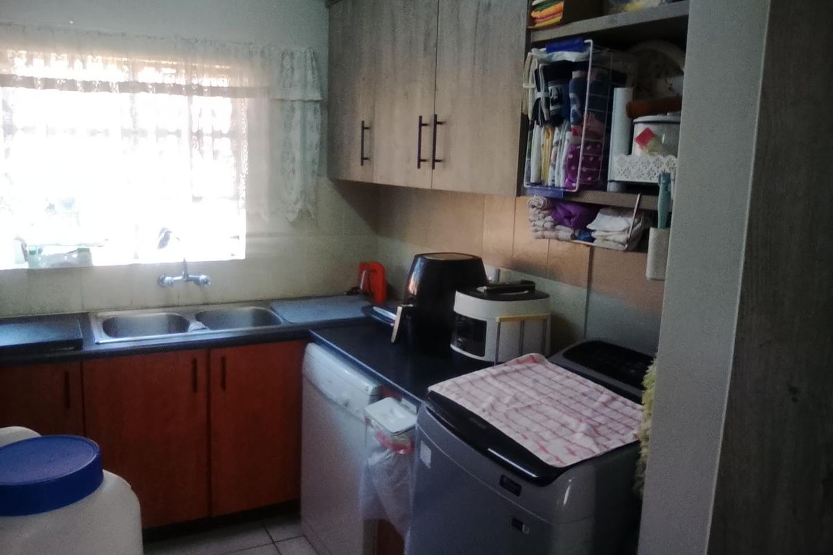 A functional kitchen area featuring laminate cabinetry, double bowl sink, and tiled splashback, providing essential utility and storage space.