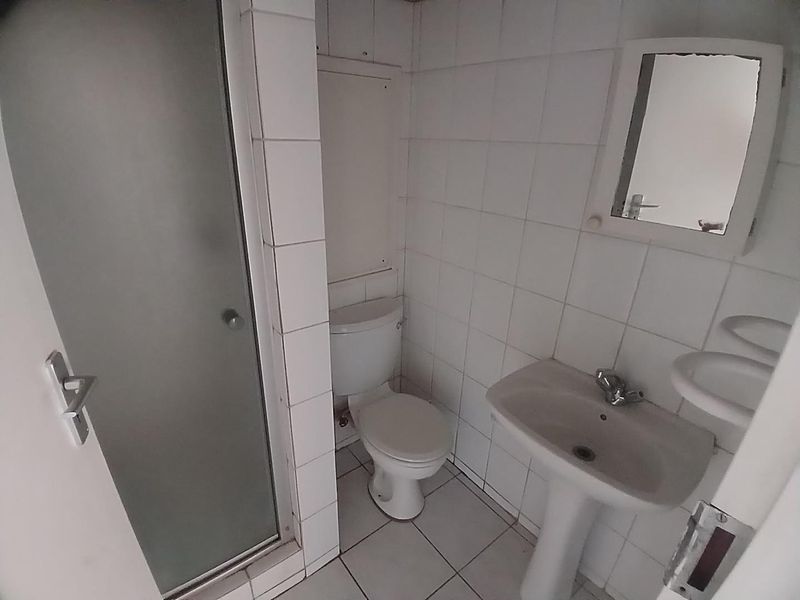 A compact bathroom featuring a shower enclosure, pedestal basin, and toilet with white tiled finishes throughout.