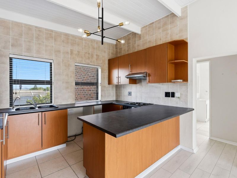 A functional kitchen featuring wood-finish cabinetry, dark laminate countertops, a built-in hob with extractor, and tiled finishes under an exposed beam ceiling.