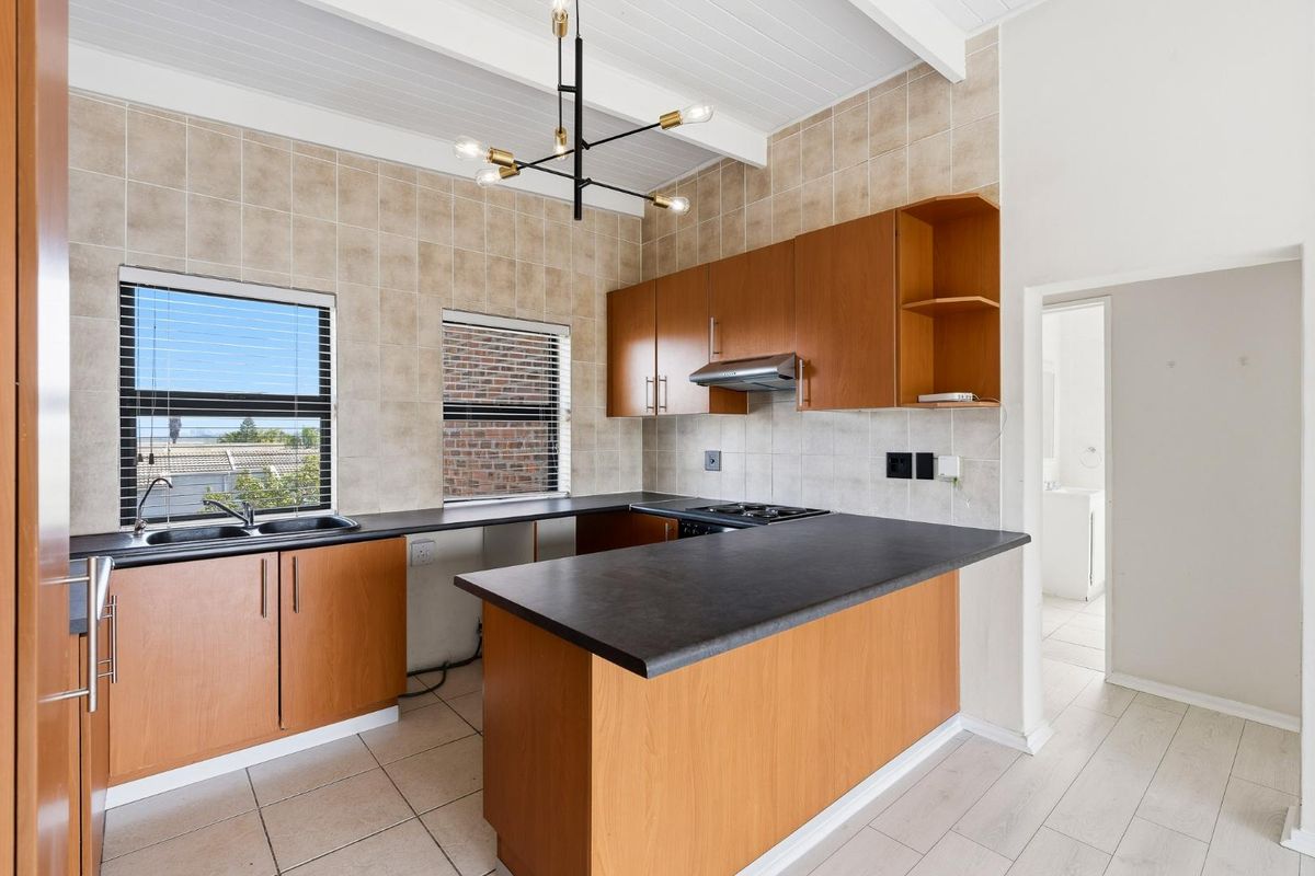A functional kitchen featuring wood-finish cabinetry, dark laminate countertops, a built-in hob with extractor, and tiled finishes under an exposed beam ceiling.