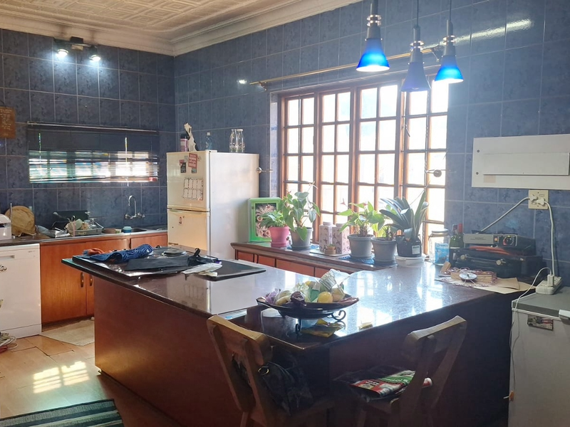 A functional kitchen featuring granite countertops, wooden cabinetry, and blue wall tiles, offering a traditional layout with ample workspace and natural light.