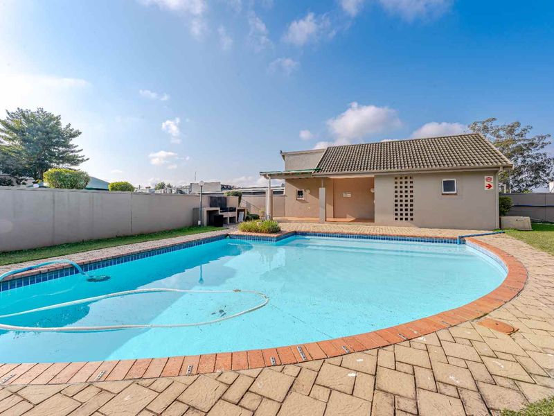 Outdoor pool area featuring a swimming pool, paved surround, and a covered entertainment structure with a built-in braai.