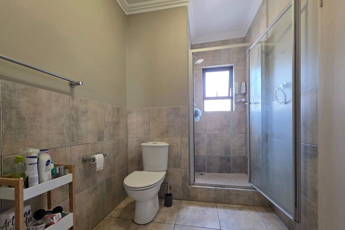 A functional bathroom featuring a glass-enclosed shower, tiled walls and flooring, and a standard toilet suite.
