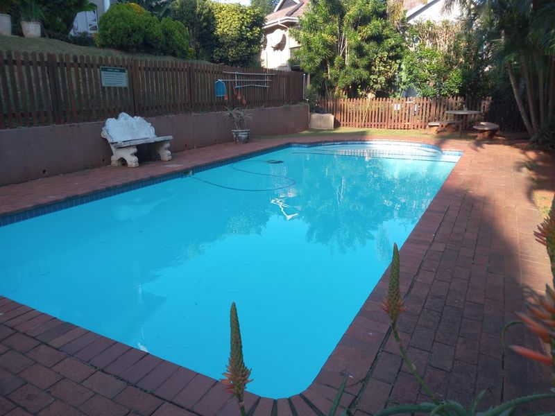 A private outdoor swimming pool area featuring brick paving, a timber boundary fence, and a retaining wall in a landscaped garden setting.