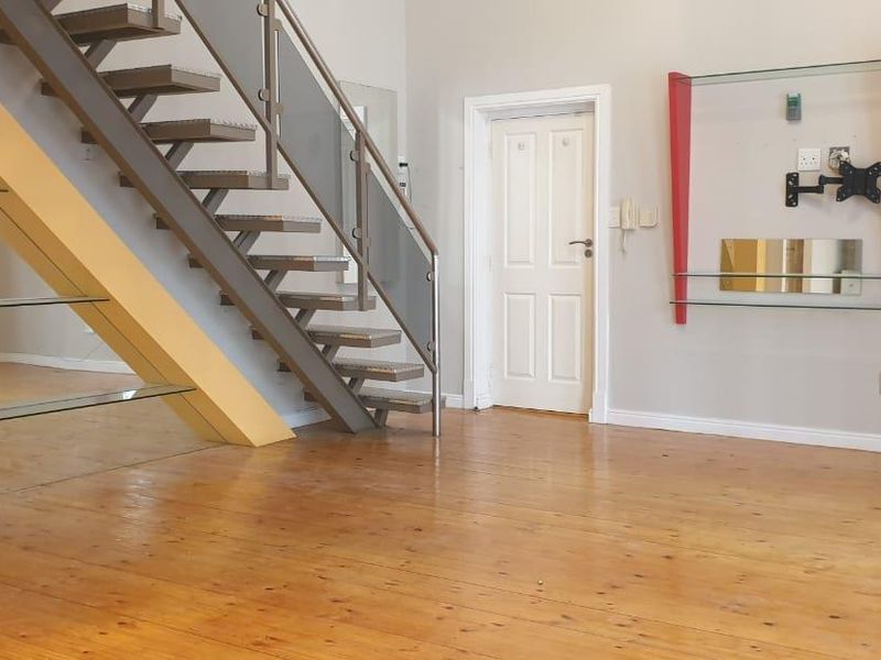 Open plan living area featuring polished wooden flooring and a modern staircase with glass balustrades and metal handrails.