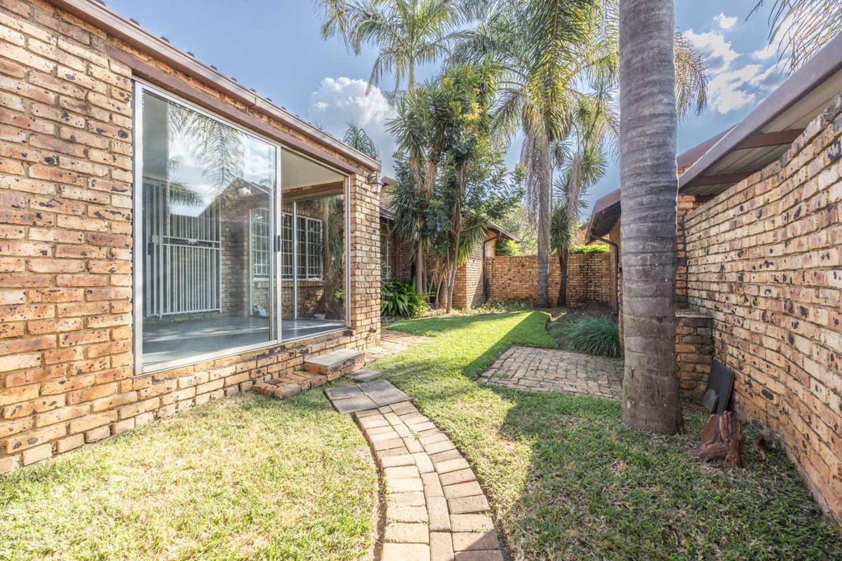 A private rear garden featuring a brick pathway, established palm trees, and a sliding glass door providing access to the townhouse interior.