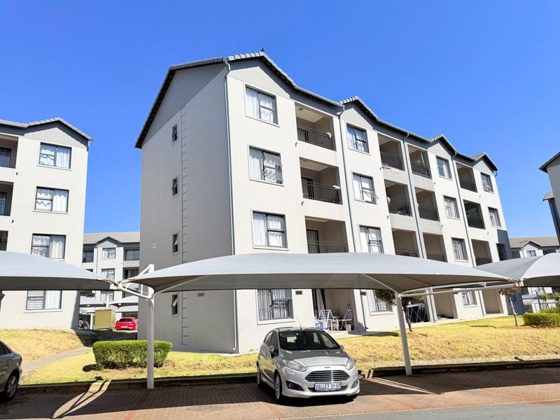 Exterior view of a multi-story apartment complex featuring covered parking bays, balconies, and well-maintained building facades under a clear sky.