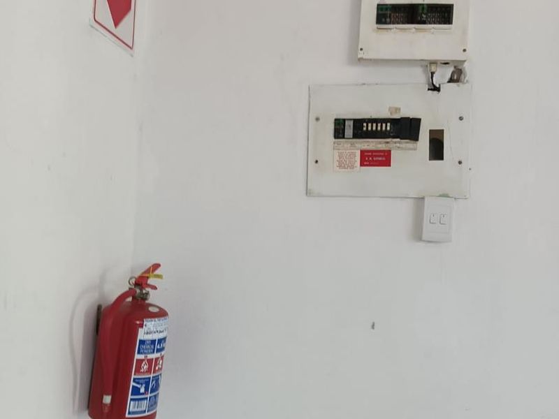 A utility area featuring a wall-mounted electrical distribution board, fire extinguisher, and safety signage.
