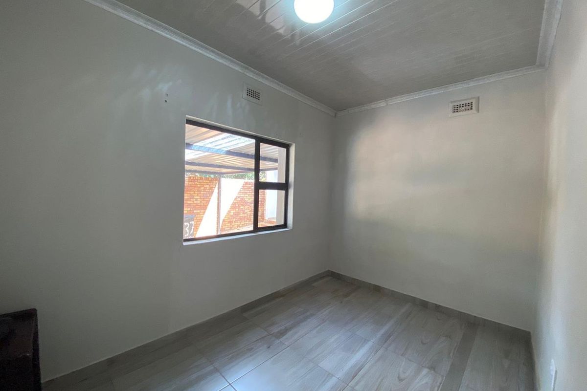 A clean, empty bedroom featuring neutral tiled flooring, a glossy ceiling finish, and a window providing natural light.